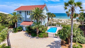 A two-story house with a red-tiled roof, a swimming pool, and a view of the beach. - Island Escape - Beach front, Private Pool, Pet Friendly and Fully Renovated! (St. George Island)