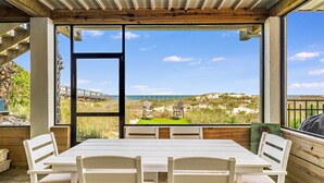 A dining area with a table and chairs, large windows offering a view of a beach and hills. - Island Escape - Beach front, Private Pool, Pet Friendly and Fully Renovated! (St. George Island)
