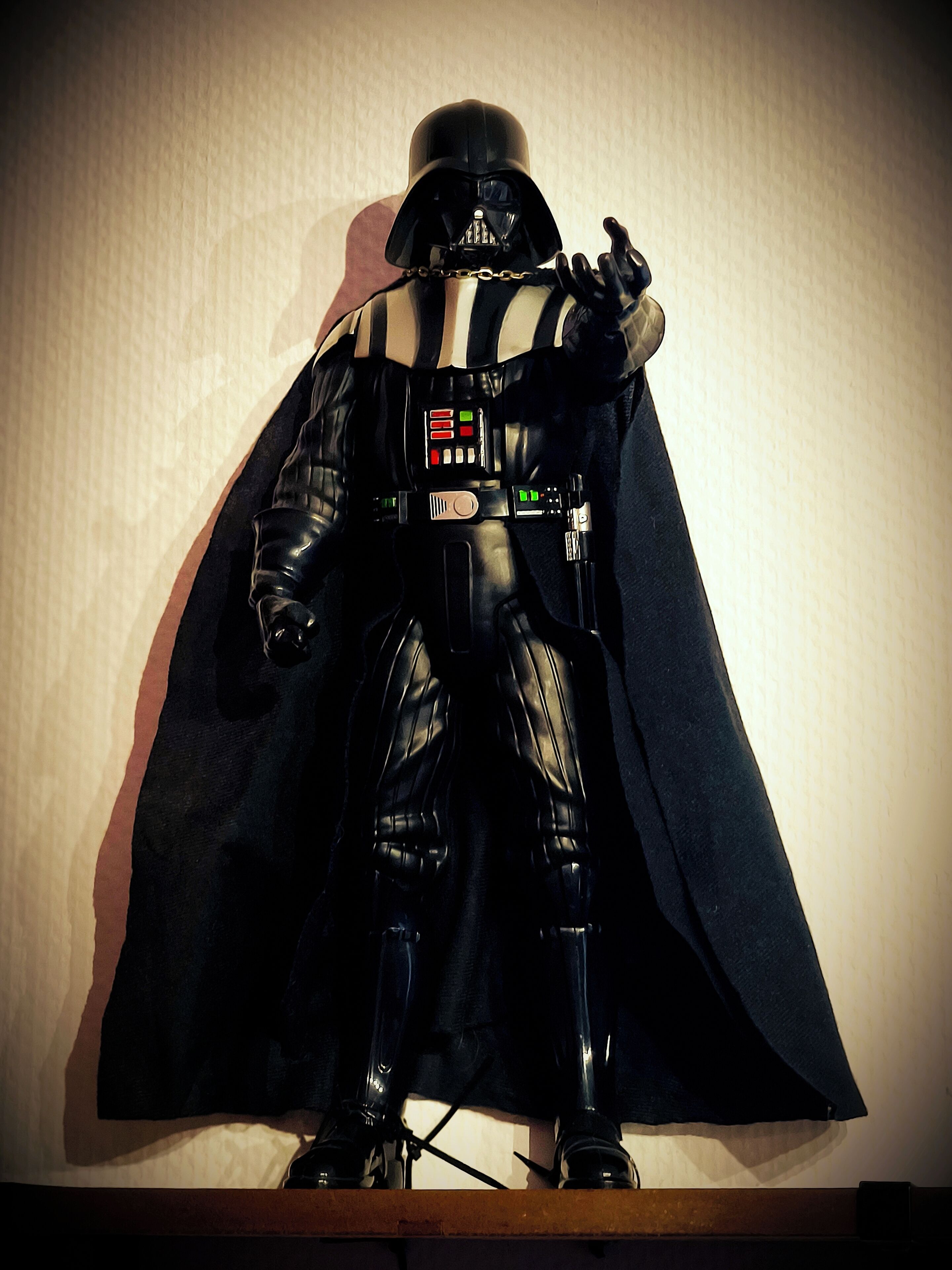 Een Darth Vader actiefiguur met cape, geplaatst voor een effen muur.