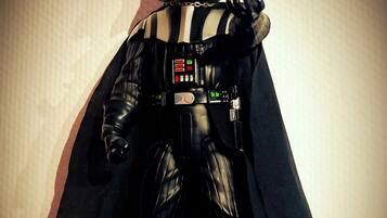 Een Darth Vader actiefiguur met cape, geplaatst voor een effen muur.