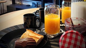 A breakfast table with a TV displaying a sports channel, a glass of orange juice, a milk jug, and a checkered lid. - Movie-themed apartment with large screen (Woustviller)