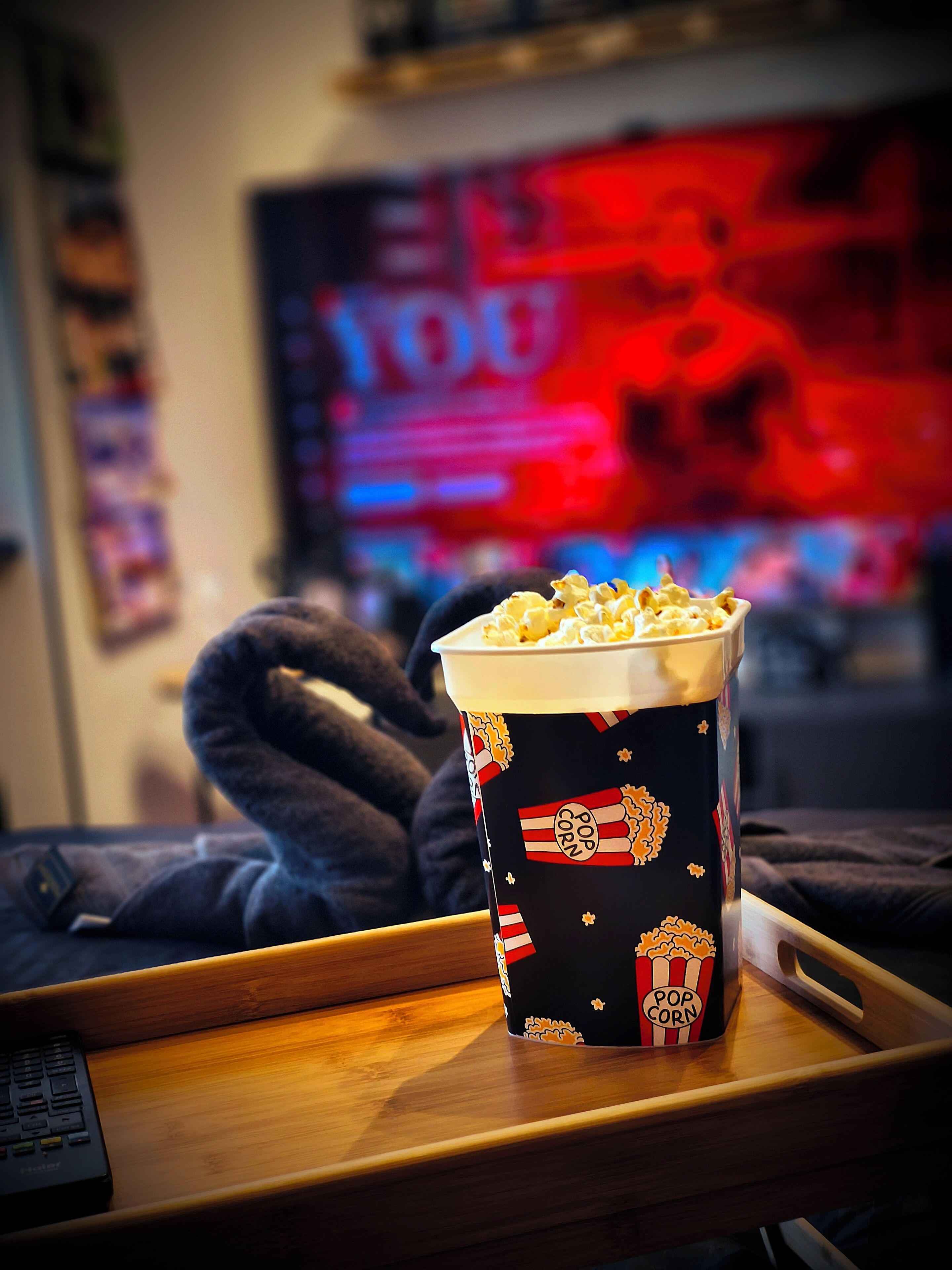 A popcorn container on a tray with a TV in the background displaying a red and blue screen.