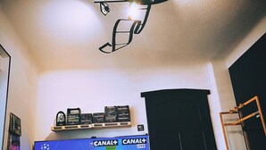 A living room with a television displaying a sports event, a ceiling fan, and a snack tray. - Movie-themed apartment with large screen (Woustviller)