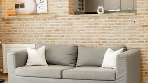 Ein graues Sofa mit Holzbeinen und weißen Kissen vor einer Backsteinwand.