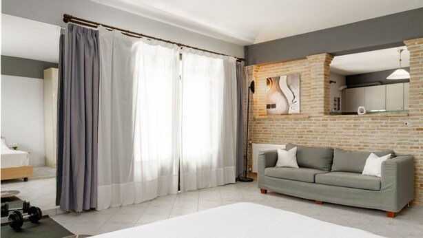 Ein modernes Schlafzimmer mit Bett, grauen Vorhängen, einem grauen Sofa, einer Wand mit Backsteinverkleidung und einem minimalistischen Design.