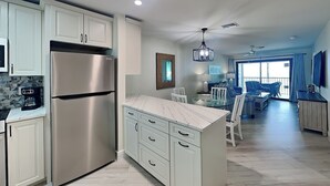 A modern kitchen with white cabinets, a stainless steel refrigerator, and a marble countertop. - Seaside Resort 507 | Fresh Renovation + Beachfront Living (Fort Myers Beach)
