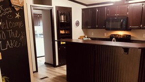 A modern kitchen with dark wooden cabinets, a central island, and a blackboard with a welcome message.