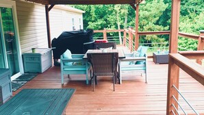 A covered outdoor deck with wooden flooring, a table, chairs, and a grill.