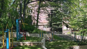 A playground with swings and climbing structures, surrounded by trees and a stone wall. - Writers hotel in Tsaghkadzor (Tsaghkadzor)