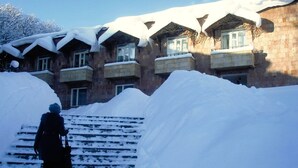 A building with multiple balconies covered in snow, steps leading up to the entrance, and a person walking down the steps. - Writers hotel in Tsaghkadzor (Tsaghkadzor)