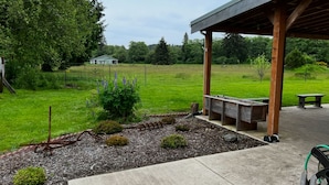 A covered outdoor area with a concrete floor, wooden benches, and a small garden with mulch and plants. - Private space in Forks with AC, high-speed Wi-Fi, covered BBQ, outdoor fire pit (Forks)