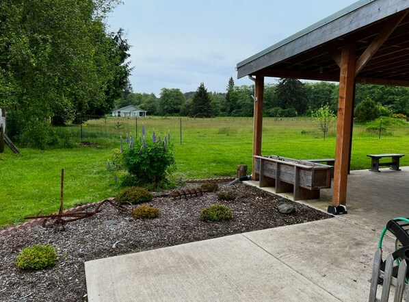 A covered outdoor area with a concrete floor, wooden benches, and a small garden with mulch and plants.