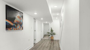 A hallway with white walls, a wooden floor, and a large abstract painting on the left. - Charming 2-bedroom apartment in fabulous Chicago with WiFi, Game Space (Chicago)