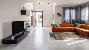 Un salon moderne avec un canapé d’angle, un téléviseur à écran plat et une grande fenêtre agrémentée de rideaux.