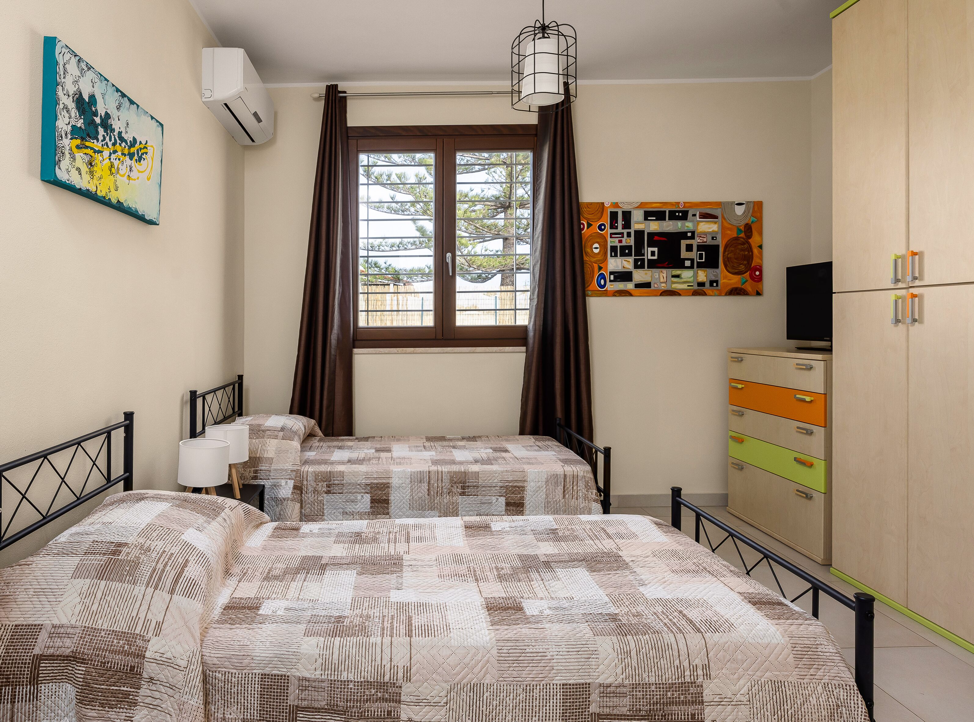 A bedroom with two beds, a window with curtains, a wall-mounted air conditioner, a ceiling light fixture, and a dresser with multiple drawers.