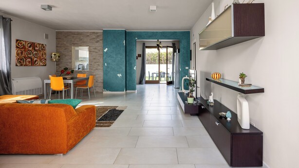 Un salon moderne comprenant un canapé, des fauteuils, une table basse et un téléviseur. On y trouve également un coin repas avec une table et des chaises, ainsi qu’une cuisine équipée d’une cuisinière et d’un évier.