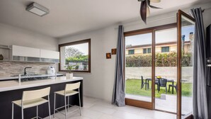 Une cuisine moderne dotée d’un îlot central, de tabourets de bar et offrant une vue sur la terrasse extérieure.