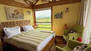 A bedroom with a wooden bed, a green armchair, and a view of the outdoors.