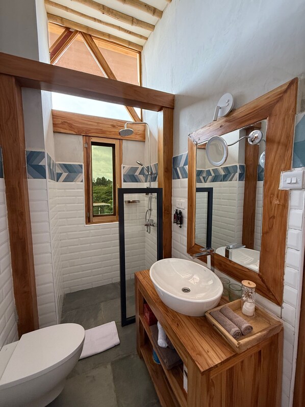 Un baño con tocador de madera, un lavabo blanco, un espejo grande y una zona de ducha.