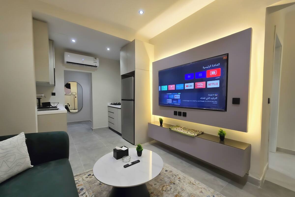 Ein modernes Wohnzimmer mit flachbildfernseher an der Wand, einem runden Couchtisch und einem Sofa.