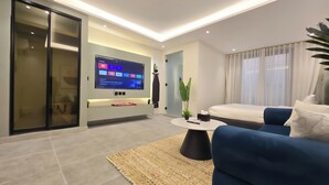 A modern living room with a flat-screen TV mounted on the wall, a sofa, a coffee table, and a sliding door closet. - Hometel NRJS B Ruh (Riyadh)