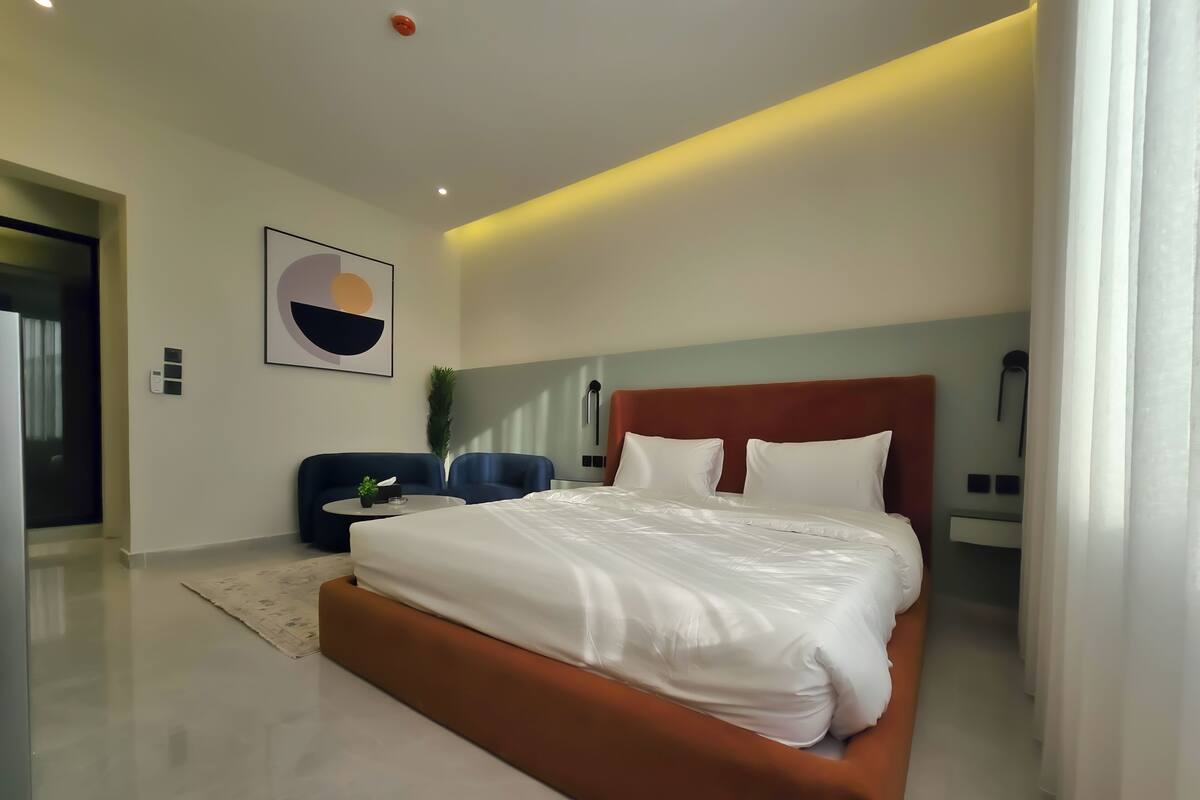 Ein modernes Hotelzimmer mit einem großen Bett, einer Sitzecke mit zwei Sesseln, einem kleinen Tisch und einem Bild an der Wand.