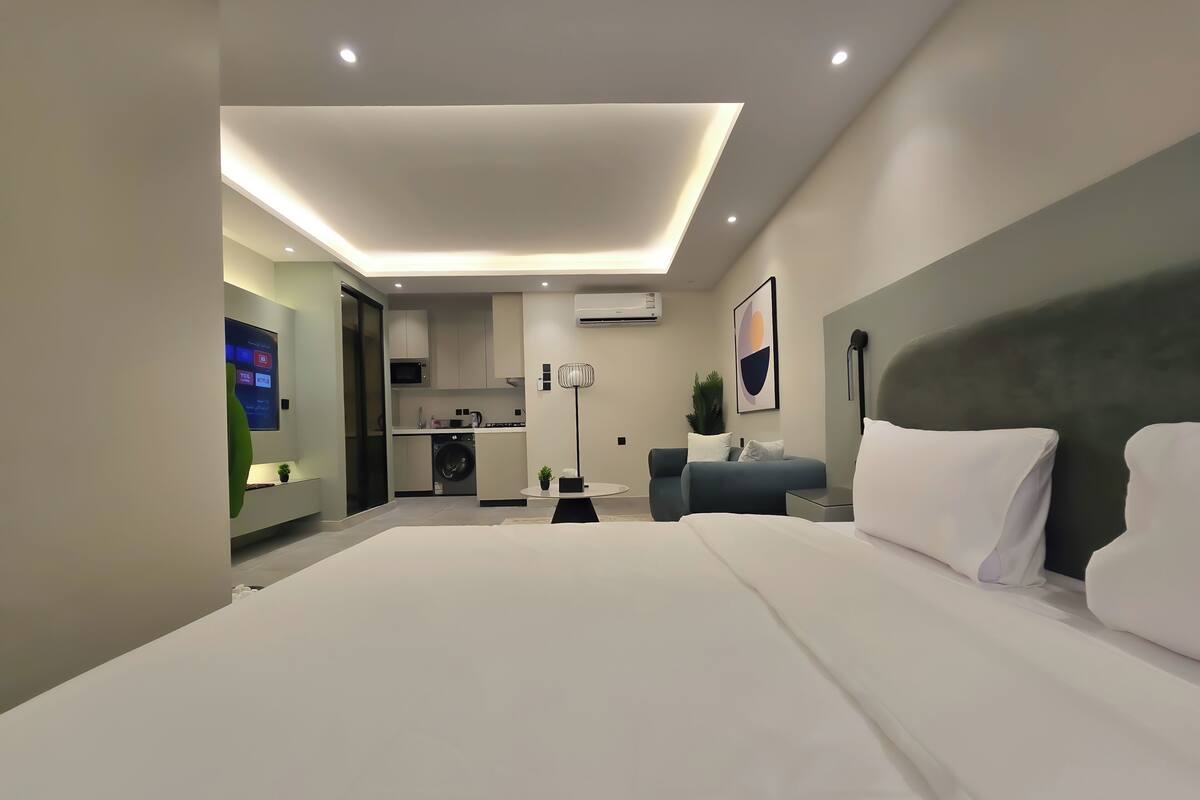 Ein modernes Hotelzimmer mit einem großen Bett, einer Sitzecke, einem Schreibtisch und einer Küchenzeile im Hintergrund.