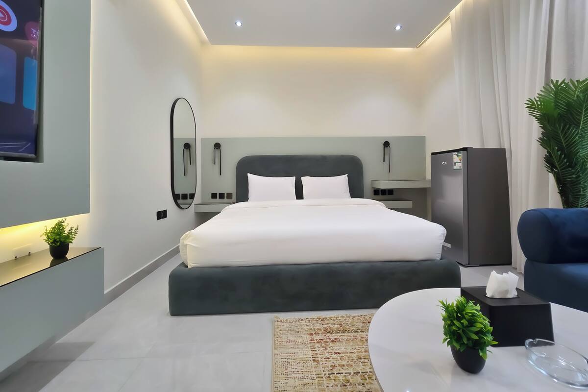 Ein modernes Hotelzimmer mit einem großen Bett, Nachttischen, einem Flachbildfernseher, einem Kühlschrank und einer Zimmerpflanze.