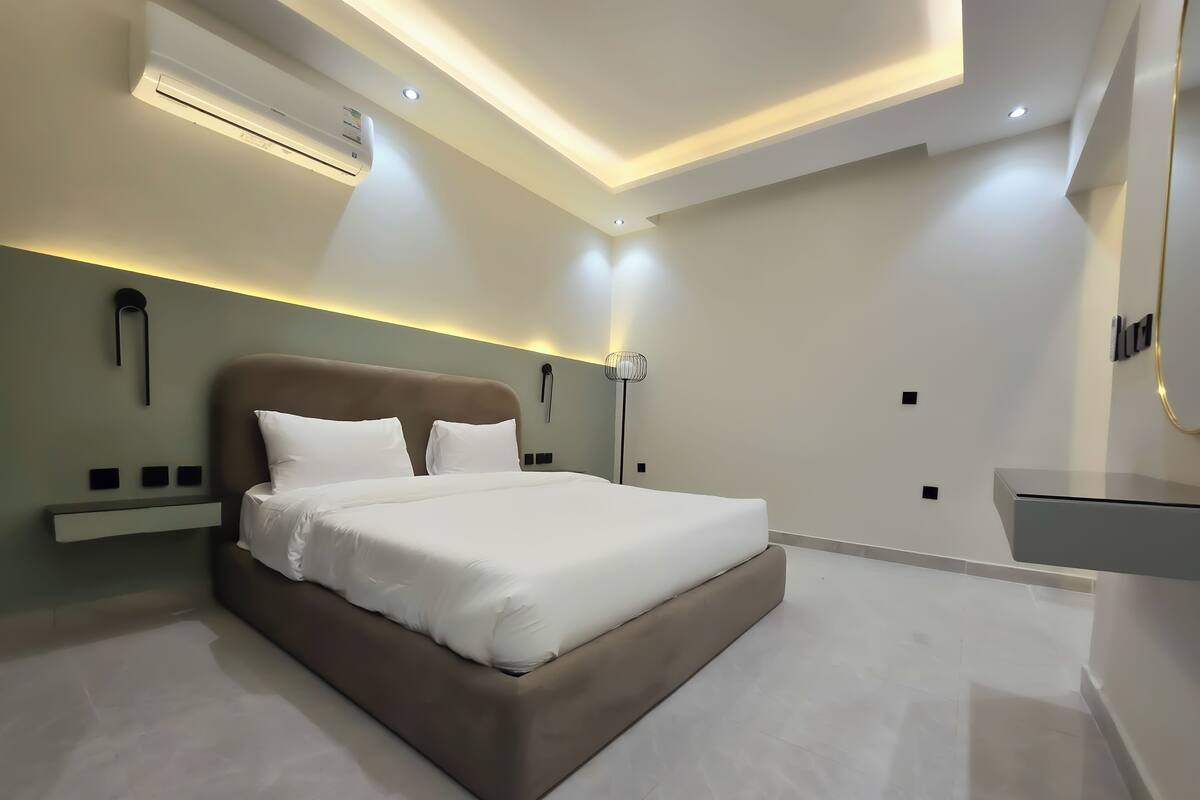 Ein modernes Schlafzimmer mit großem Bett, eingelassener Deckenbeleuchtung und integrierter Klimaanlage.