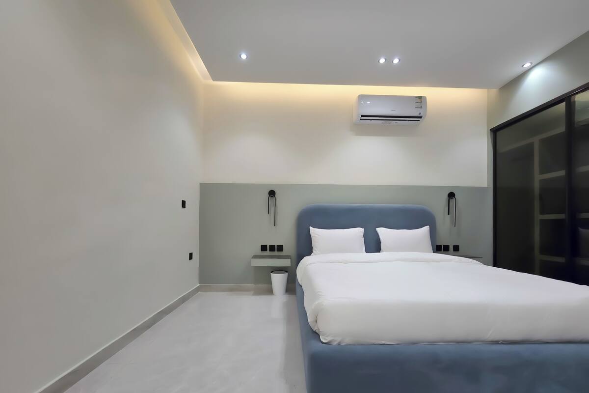 Ein modernes Schlafzimmer mit einem großen Bett, einem Nachttisch, einer Wand-Klimaanlage und einem großen Fenster.
