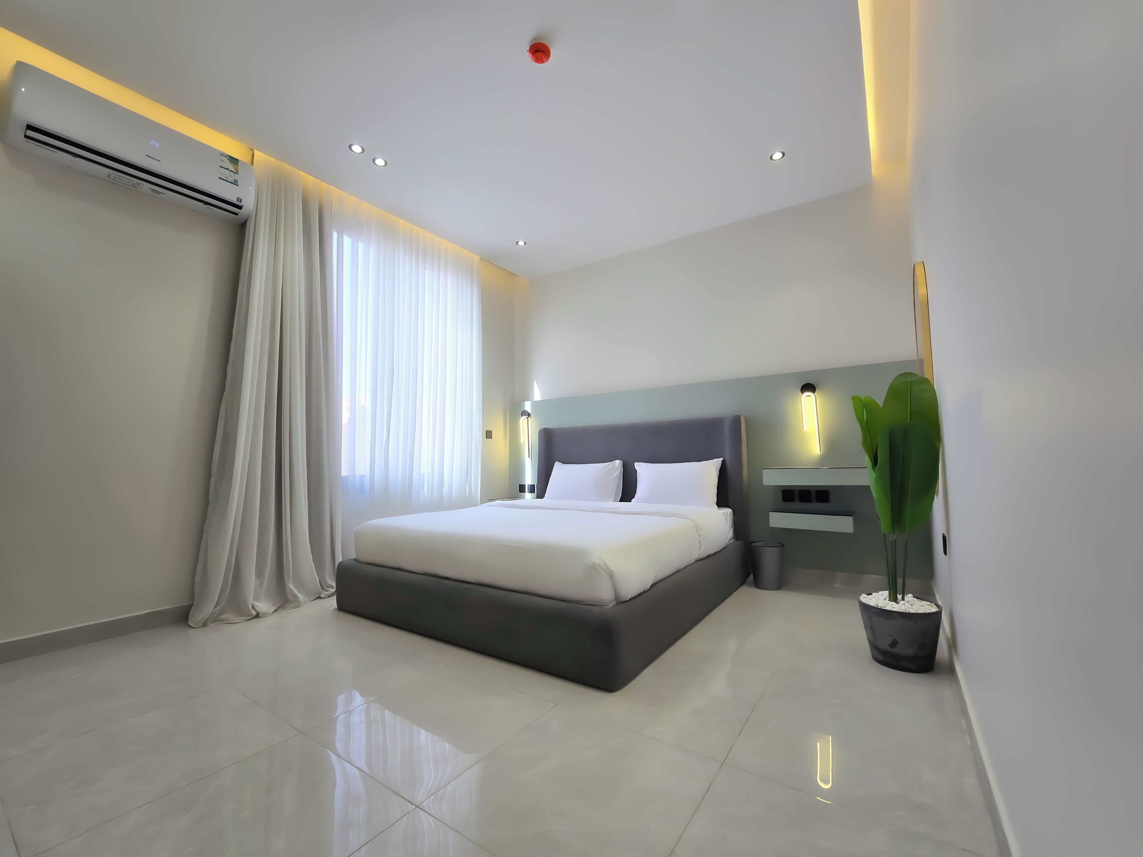 Une chambre d’hôtel moderne avec un grand lit, des tables de chevet, une plante en pot et un climatiseur fixé au plafond.