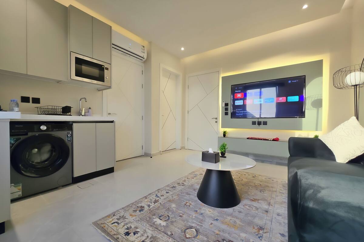 Ein moderner Wohnraum mit einer Küche, einer Waschmaschine, einem Flachbildfernseher und einem Sofa.