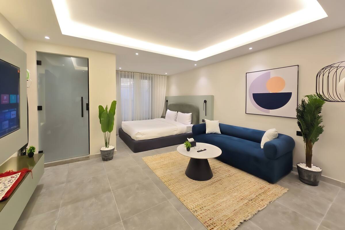 Ein modernes Hotelzimmer mit Bett, blauem Sofa, Couchtisch und Fernseher.