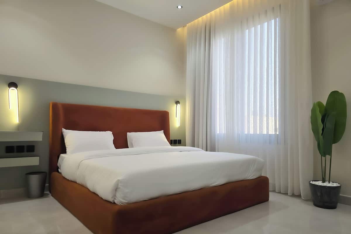 Ein modernes Schlafzimmer mit einem großen Bett, weißer Bettwäsche und einem Topf mit Pflanze.