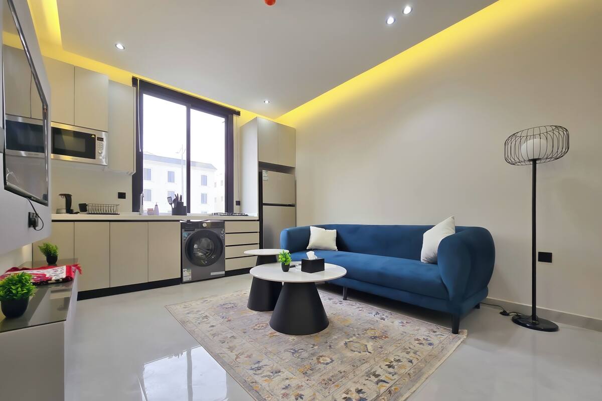 Eine moderne Wohnung mit Küche, einem blauen Sofa, einem kleinen runden Tisch und einer Stehlampe.