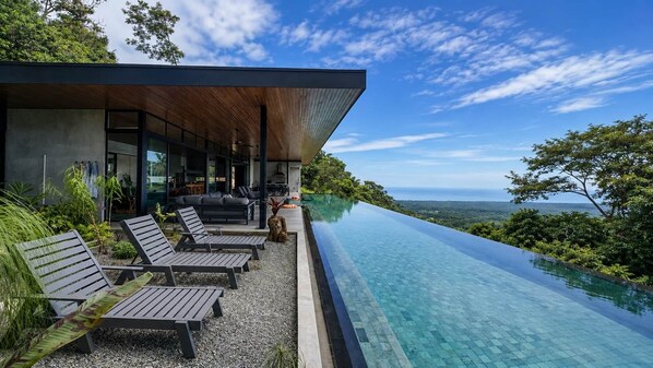 A modern building with a pool extending to the edge of a cliff overlooking a landscape.