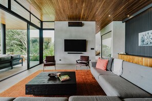 A modern living room with a large TV, comfortable seating, and a view of greenery outside.
