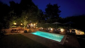 Un espace extérieur avec piscine, aménagé pour la nuit, comprenant des chaises longues et un barbecue.