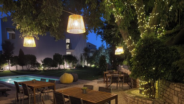 Un espace extérieur aménagé en terrasse, avec des tables et des chaises, une piscine et des guirlandes lumineuses.