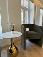 Egy modern nappali, melyben egy kerek márványasztal, egy sötétszürke kanapé és egy virágzó orchidea található cserépben.