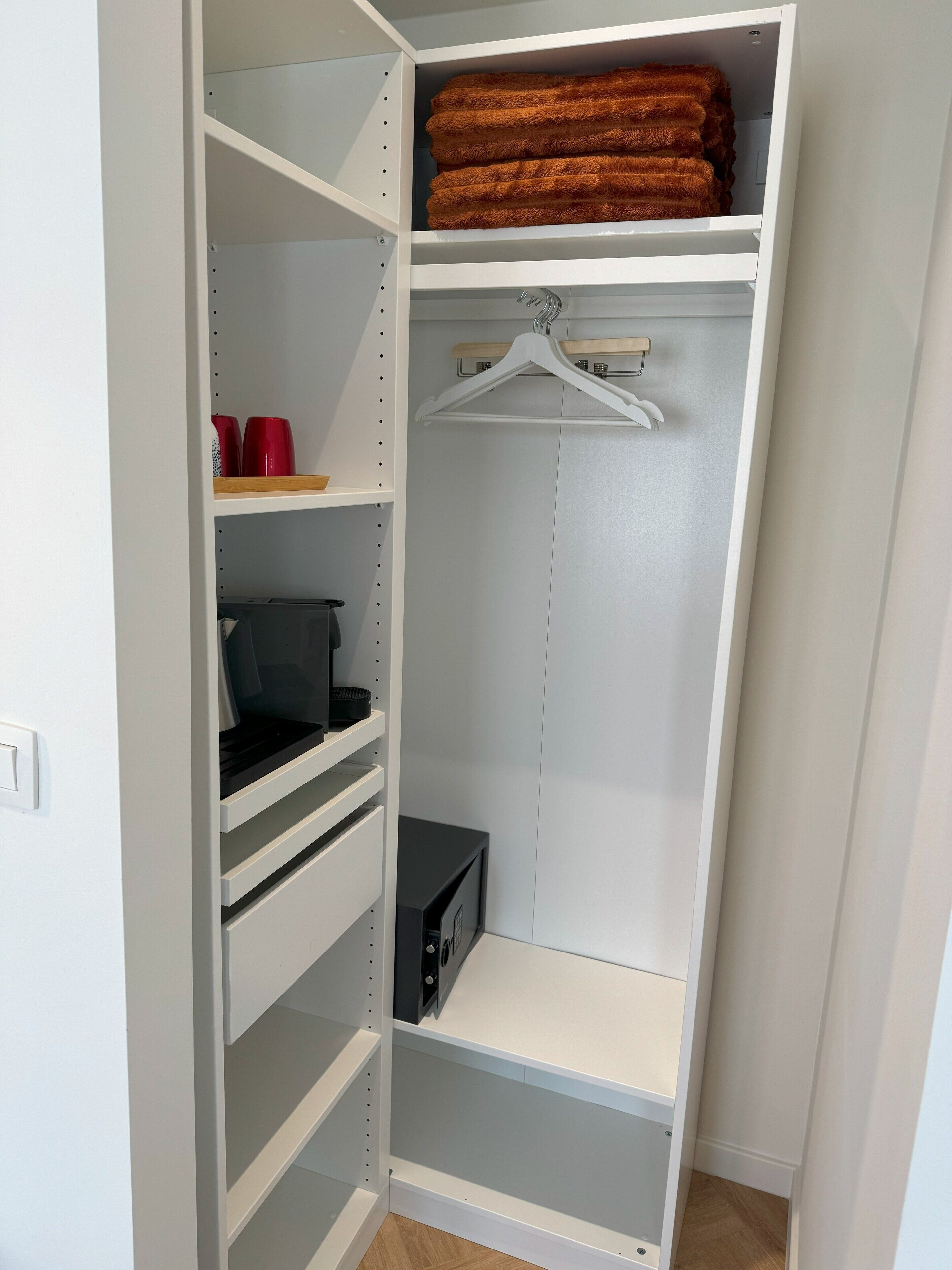 A white closet with multiple shelves, a hanging rod, and a microwave.