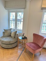 Una sala de estar con un sofá redondo gris, un sillón rosa y una pequeña mesa redonda con una planta.