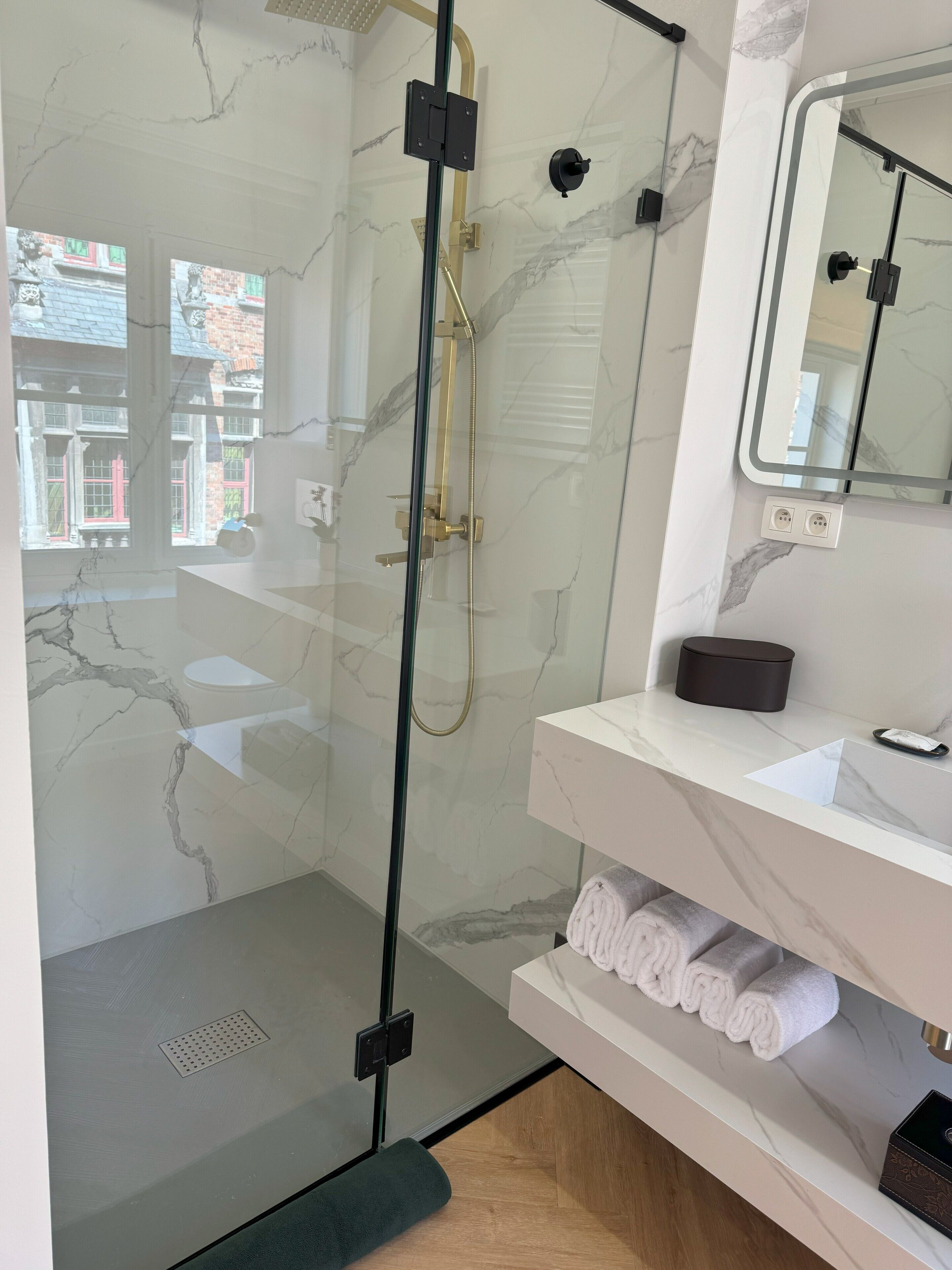 A modern bathroom with a glass-enclosed shower, a marble-tiled wall, a white sink, and a mirror above the vanity.
