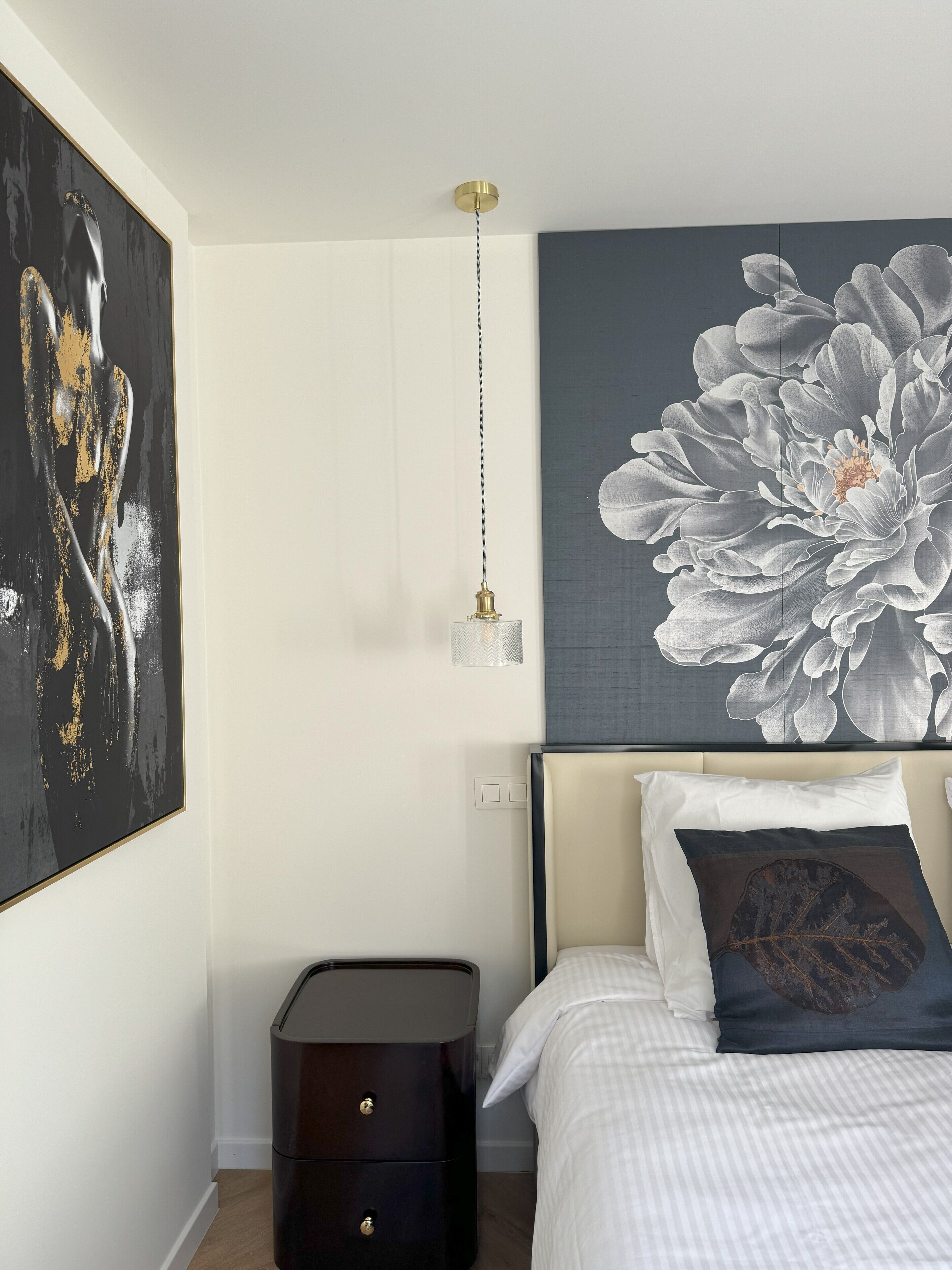 Ein Schlafzimmer mit großem Blumenbild an der Wand, einem Nachttisch und einem Bett mit Kissen.