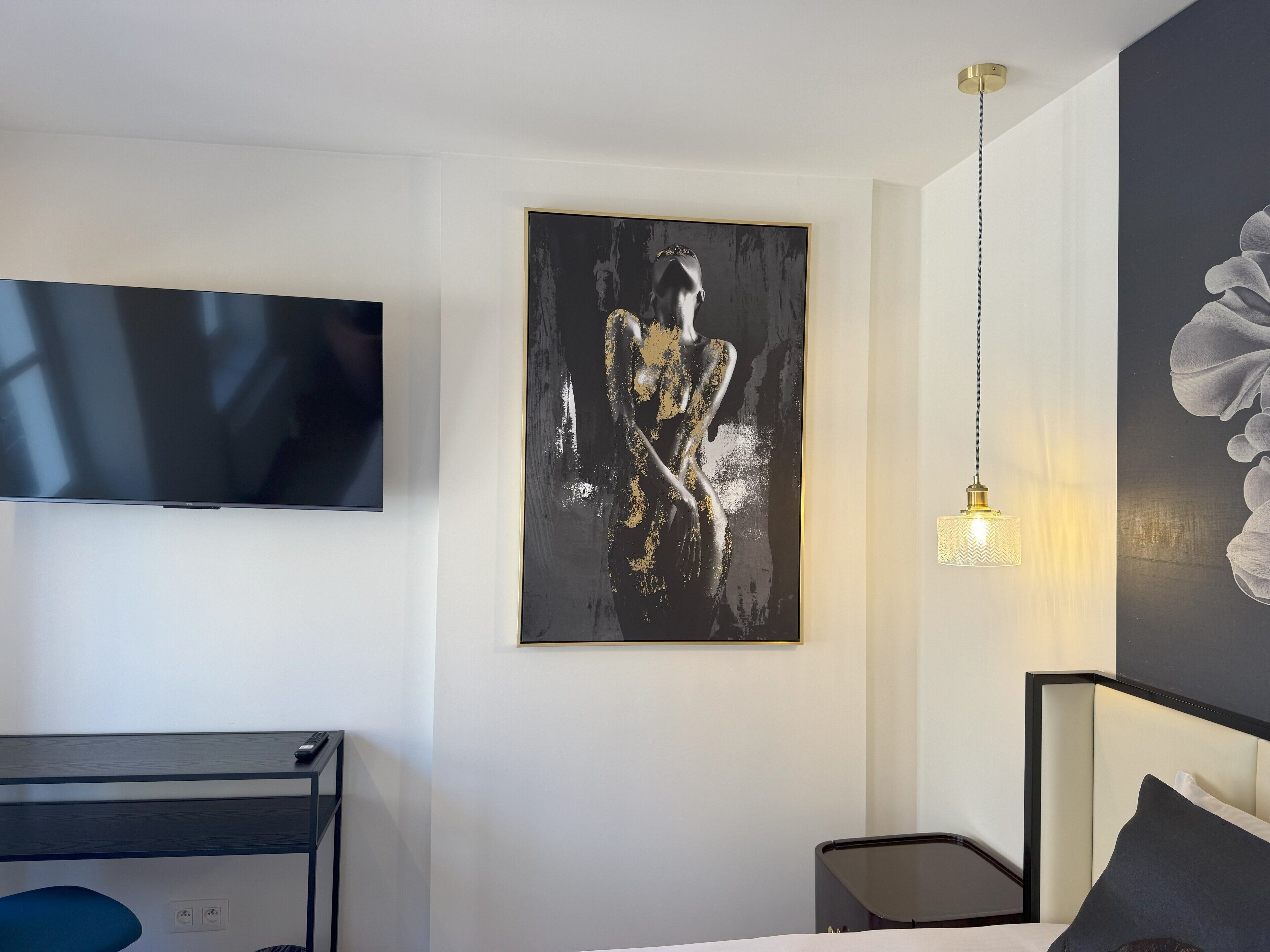 A modern hotel room with a flat-screen TV, a large abstract painting, a bedside lamp, and a bed with a headboard.