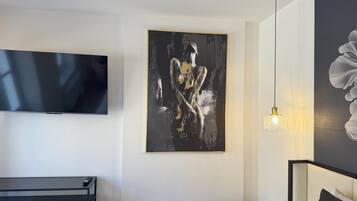 A modern hotel room with a flat-screen TV, a large abstract painting, a bedside lamp, and a bed with a headboard.