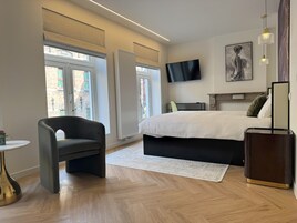 Egy modern hálószoba, melyben egy nagy ágy, egy síkképernyős televízió található, és a nagy ablakokon keresztül a városra nyílik kilátás.