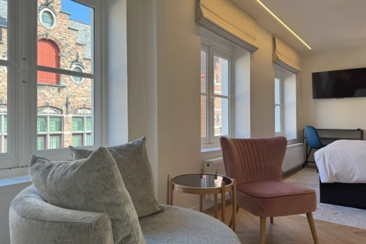 Une chambre d’hôtel moderne dotée d’une grande fenêtre, d’une table ronde, d’un fauteuil confortable, d’un lit et d’un téléviseur à écran plat fixé au mur.