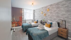 Ein modernes Schlafzimmer mit zwei Betten, einer Ziegelwand, einem Stadtbild-Wandgemälde und einem Nachttisch mit Lampe.
