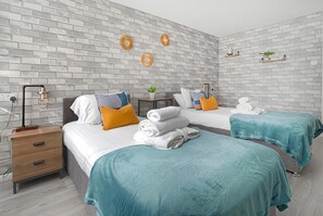 Un dormitorio moderno con dos camas, una mesita de noche, una lámpara y detalles decorativos en la pared.